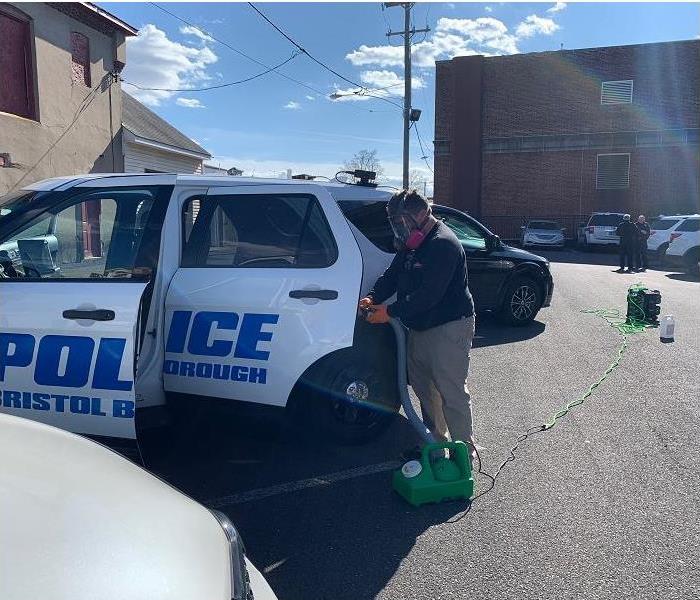 SERVPRO technician, wearing PPE, disinfecting police car